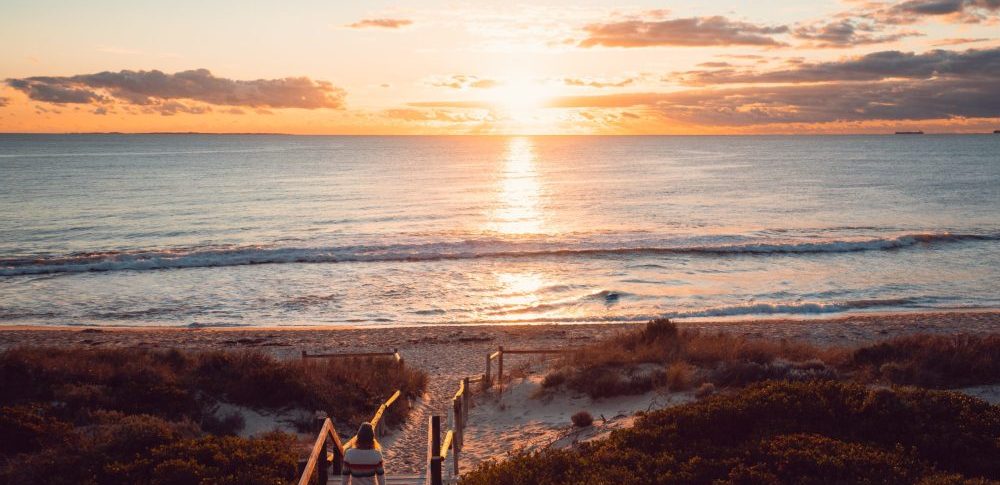 Woman walking down beach staircase at sunset